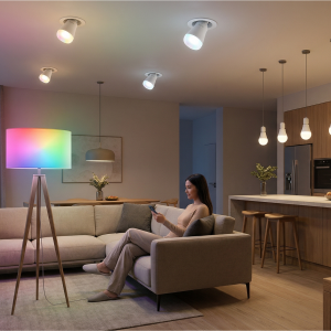 Osoba siedząca na sofie trzymająca telefon, otoczona kolorowym oświetleniem LED, w salonie z drewnianymi akcentami